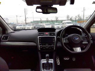 Салон Subaru Levorg 2017: панель приборов, руль и мультимедиа, вид через лобовое стекло на парковку аукциона, аккуратный интерьер.