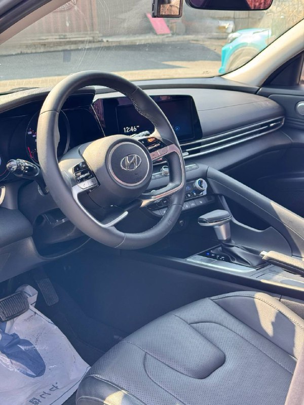 Вид салона и рулевой колонки Hyundai Avante (Elantra) 2021 со стороны водителя; показаны сиденье, руль и часть торпедо.