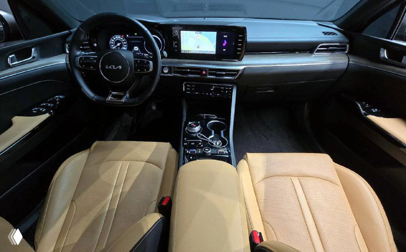 Интерьер KIA K5 2022: передняя панель, центральный дисплей и цифровая приборная панель, бежевые сиденья и центр консоли видны крупным планом.
