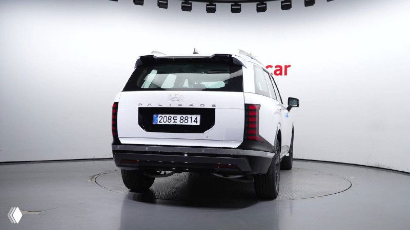 Задняя часть белого Hyundai Palisade 2025 с видимым номером дилерской площадки, легковой внедорожник в стендах шоурума Encar