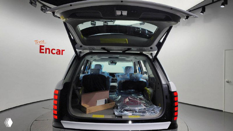 Открытый багажник Hyundai Palisade 2025 с грузом и упаковками внутри на фоне студийной площадки Encar, емкий багажный отсек