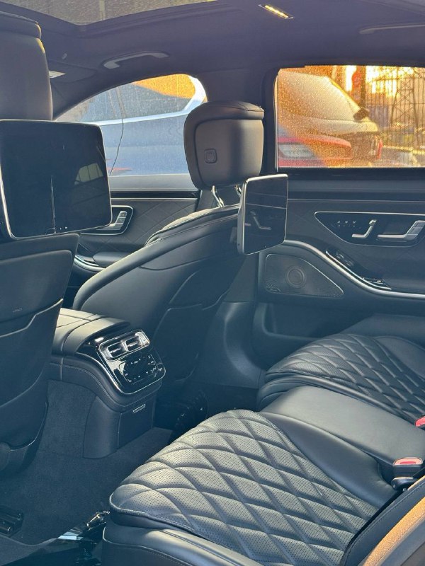 Задний ряд салона Mercedes S 350d: чёрные кожаные сиденья, мониторы за передними креслами и центральный тоннель с сопутствующими элементами управления.