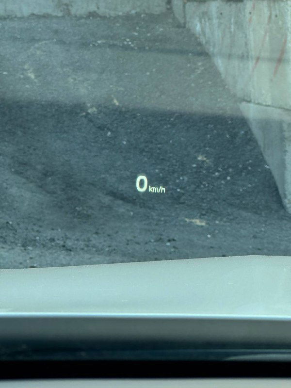 Крупный план проекции HUD на лобовом стекле KIA K5, отображение скорости 0 km/h на фоне дорожного покрытия и стекла.