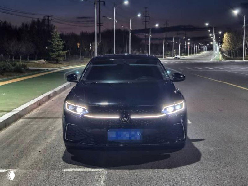 Фронтальный вид Volkswagen Passat рестайлинг 2022 на ночной дороге, симметричное освещение фар и номерной знак синим фильтром.