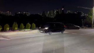 Темноватый ночной кадр автомобиля на подъезде к автовозу, видны дорожное покрытие и освещение, процесс загрузки в Южной Корее.