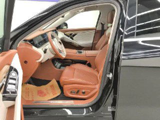 Открытая передняя дверь Voyah Free и вид на водительское сиденье с коричневой кожей, регулировки сиденья и дверная панель с элементами управления.