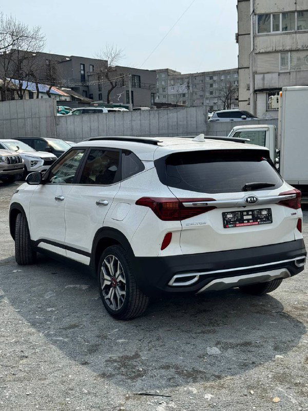 KIA Seltos белого цвета — вид сзади и в три четверти, заметна задняя оптика, форма кузова и бампер, автомобиль на открытой стоянке.