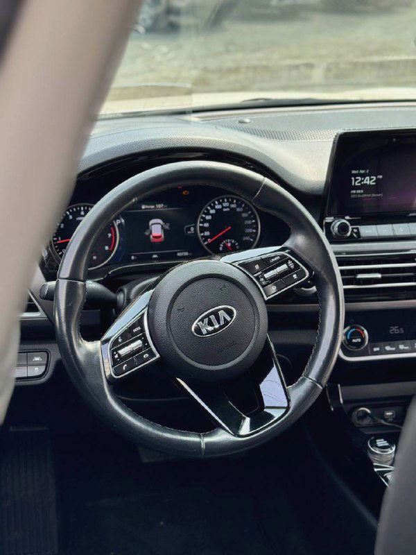 Рулевое колесо и приборная панель KIA Seltos: крупный план мультируля, тахометра, спидометра и центрального дисплея на переднем плане.