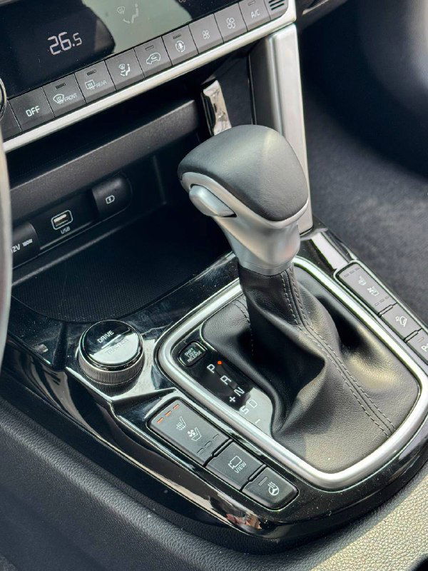 Селектор автоматической коробки передач KIA Seltos в центре туннеля: крупный план ручки, поручней и кнопок режима движения рядом с подстаканниками.