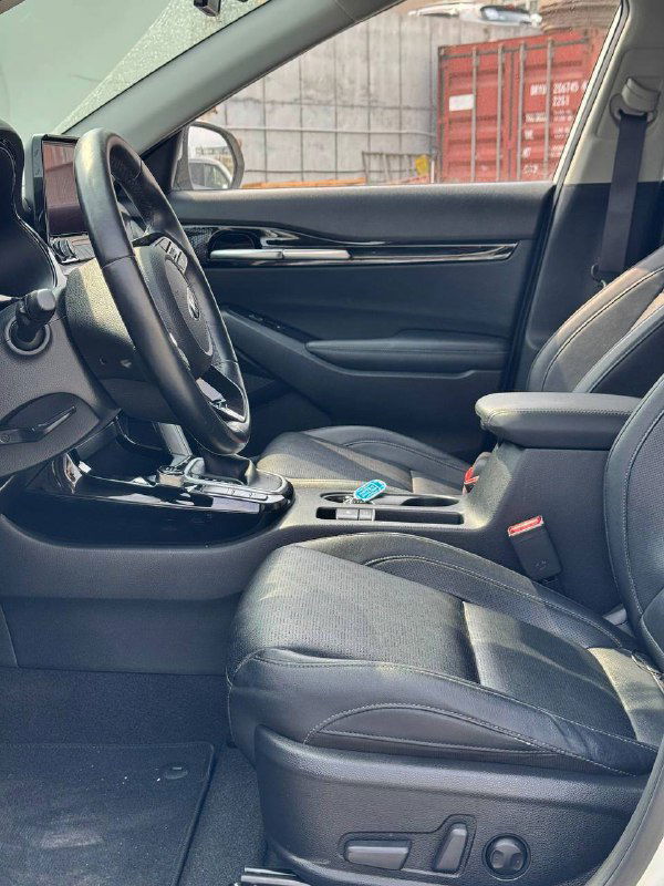 Передние сиденья и часть салона KIA Seltos: вид со стороны двери, состояние обивки, передняя консоль и место водителя с регулировками.