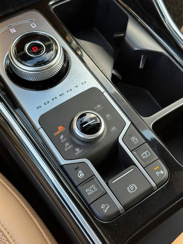 Ручка селектора режимов и кнопки ассистентов в KIA Sorento — крупный план кнопок парковки, ручного тормоза и режимов привода.