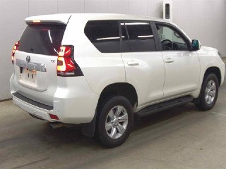 Задний и боковой ракурс белого Toyota Prado 2022 в помещении осмотра — видны фонари, багажная дверь и профили крыла и порога.