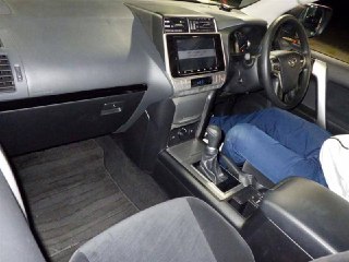 Интерьер Toyota Prado 2022: передняя панель, центральная консоль, селектор АКПП и сиденья в серой обивке, вид с пассажирской стороны.