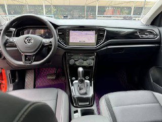 Салон Volkswagen T‑Roc: вид на рулевое колесо, центральную мультимедийную панель, контрольные приборы и рычаг переключения передач в передней части салона.