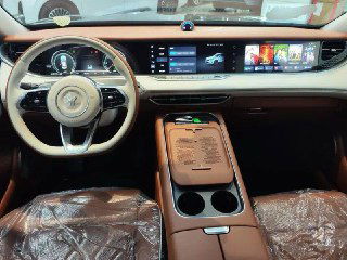 Салон Voyah Free: передняя панель, рулевое колесо и центральный тоннель с подстаканниками, коричневая отделка и защитные плёнки на сиденьях.