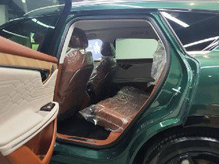 Вид на вторые ряды сидений Voyah Free: задняя часть салона с коричневой обивкой, защитные плёнки на подголовниках и достаточно места для пассажиров.