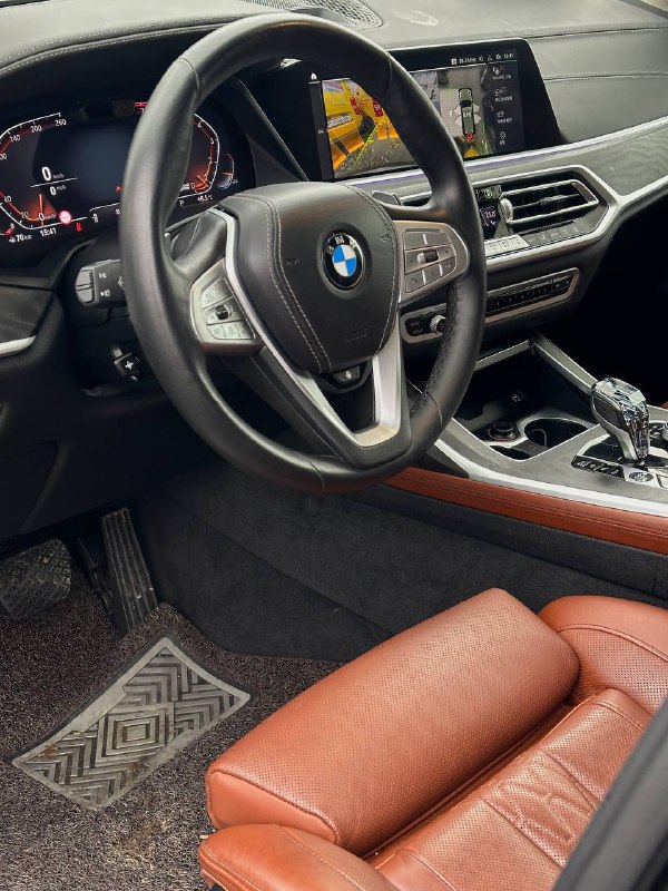 Салон BMW X7: вид на рулевое колесо, приборную панель и центральную консоль — коричневая кожа, система управления и навигация в кадре.