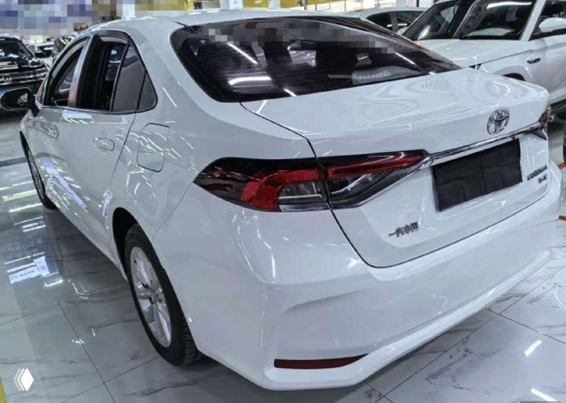 Вид сзади белой Toyota Corolla 2021 в выставочном зале: форма задних фонарей, багажник и общие пропорции кузова для оценки состояния перед экспортом.