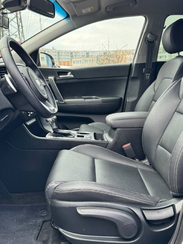 Передние сиденья KIA Sportage: обзор салона со стороны пассажирского сиденья, видны сидения, центральный подлокотник и общая компоновка интерьера