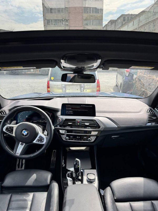 Вид торпедо и мультимедийного экрана BMW X3 — панель приборов, руль и часть лобового стекла, интерьер спереди