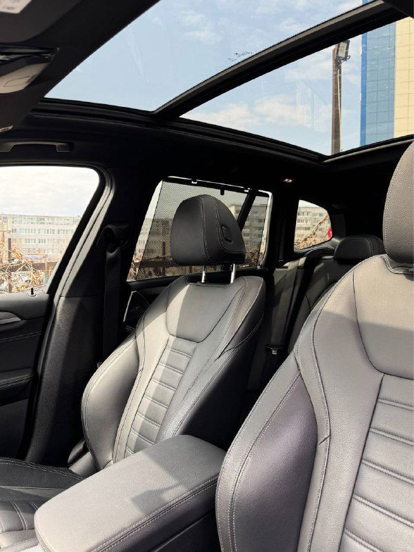 Панорамная крыша BMW X3 крупным планом, вид открытого люка и передних сидений с кожаной отделкой в дневном свете