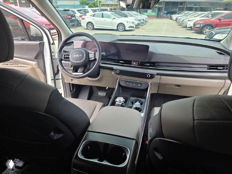 Интерьер KIA Carnival 2024 — общий вид салона с передней панелью, рулём, мультимедийным экраном и центральной консолью крупным планом.