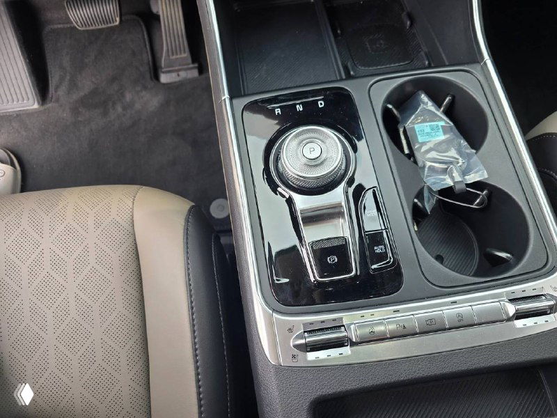 Крупный план центральной консоли KIA Carnival 2024 — селектор трансмиссии, подстаканники и элементы управления, чистая отделка.