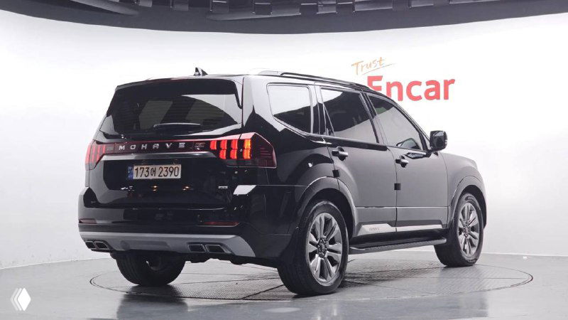 KIA Mohave 2022 чёрного цвета — задний трёхчетвертной ракурс в выставочном помещении, видны фонари, бампер и профиль автомобиля.