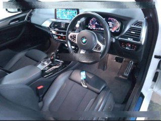 Интерьер BMW X3 2020: салон водителя, кожаное кресло, руль с логотипом BMW, центральная консоль с мультимедиа и коробкой передач.