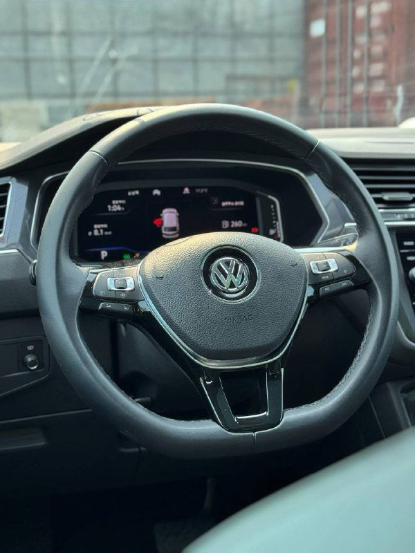 Рулевое колесо Volkswagen Tiguan с логотипом бренда и цифровой приборной панелью на фоне салона, видна центральная часть панели водителя.