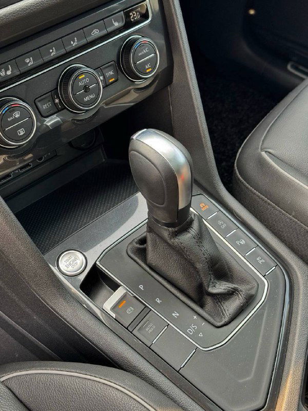 Рычаг автоматической коробки передач Volkswagen Tiguan, крупный план селектора передач и кнопок рядом с ним, видна текстура облицовки салона.