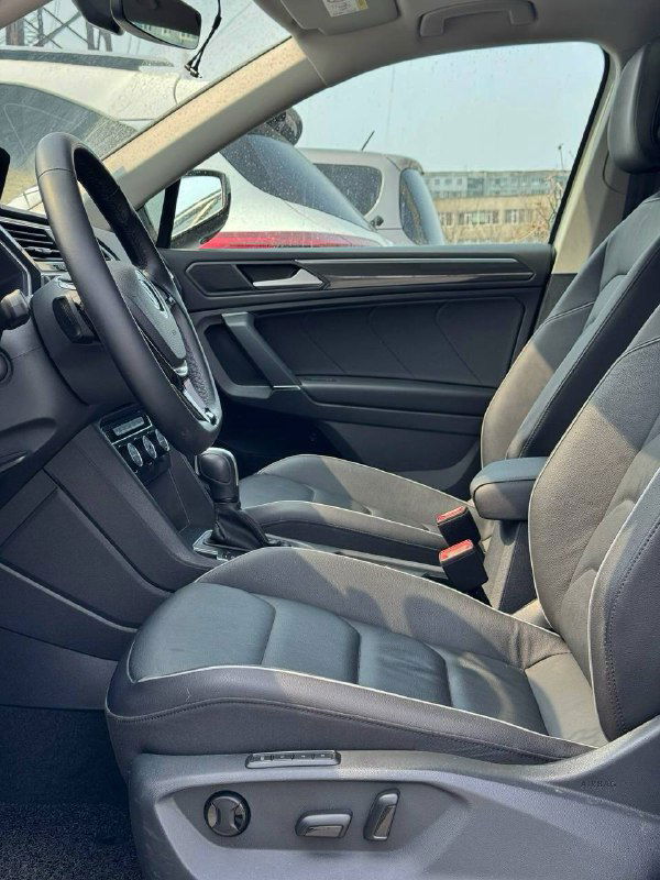 Передние сиденья и часть водительского пространства Volkswagen Tiguan 2020: обивка сидений, подлокотник и панель двери, общий вид интерьера.