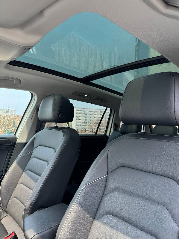 Панорамный люк и передняя часть салона Volkswagen Tiguan, видны сиденья, обивка и стеклянная крыша, обеспечивающая свет в интерьере автомобиля.