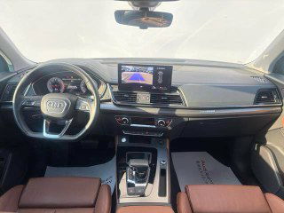 Салон Audi Q5L: вид на рулевую колонку, центральную консоль и экран мультимедиа, коричневые кожаные сиденья и ручка КПП.