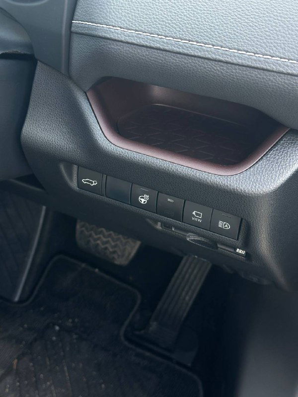 Фрагмент нижней части торпеды Toyota RAV4 2021: блок кнопок слева от руля, отделка поручня, вид на педали и грязевую защиту в районе водительского места.