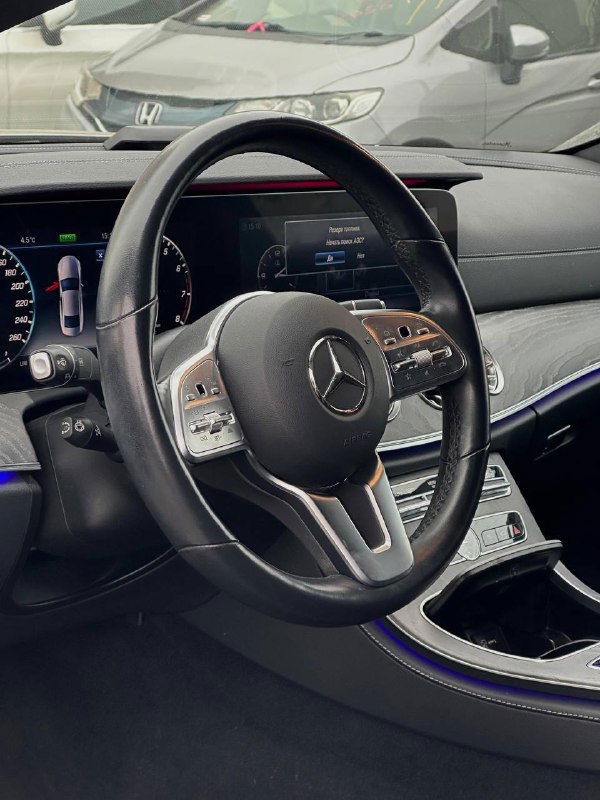 Интерьер Mercedes CLS450: крупный план рулевого колеса, мультируль, приборная панель и мультимедийный экран, отделка кожей и подсветка AMG Line, 3.0л.