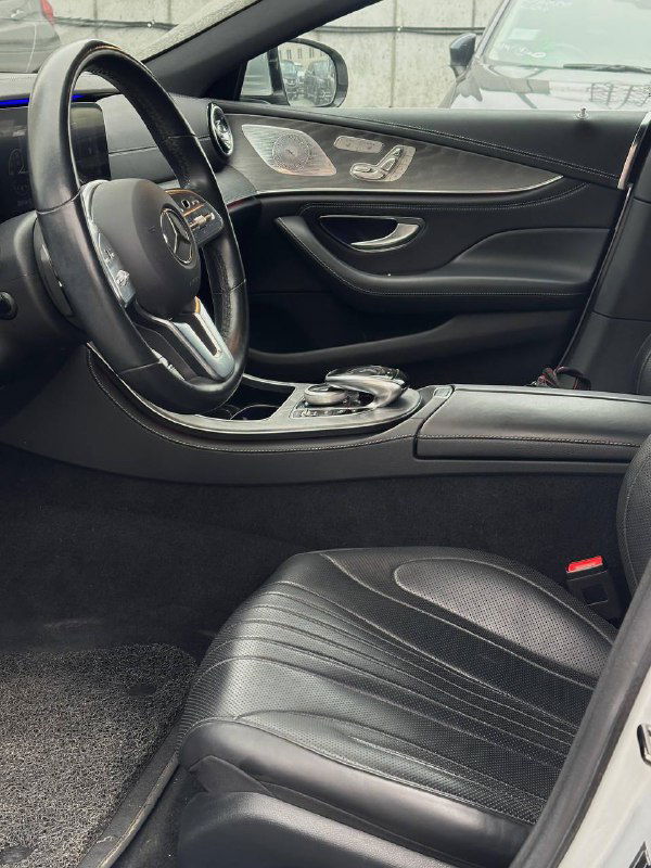 Вид на переднюю часть салона Mercedes CLS450: водительское сиденье, центральный тоннель и панель двери, кожа с прострочкой и комфортные посадочные места для клиента.