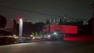 Ночной кадр с автовозом, в фокусе видна боковая часть прицепа и габаритные огни, машины уже размещены на верхней палубе.