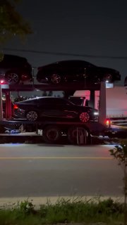 Вертикальный кадр автопоезда с несколькими легковыми автомобилями на двух уровнях платформы, снято ночью с близкого расстояния.