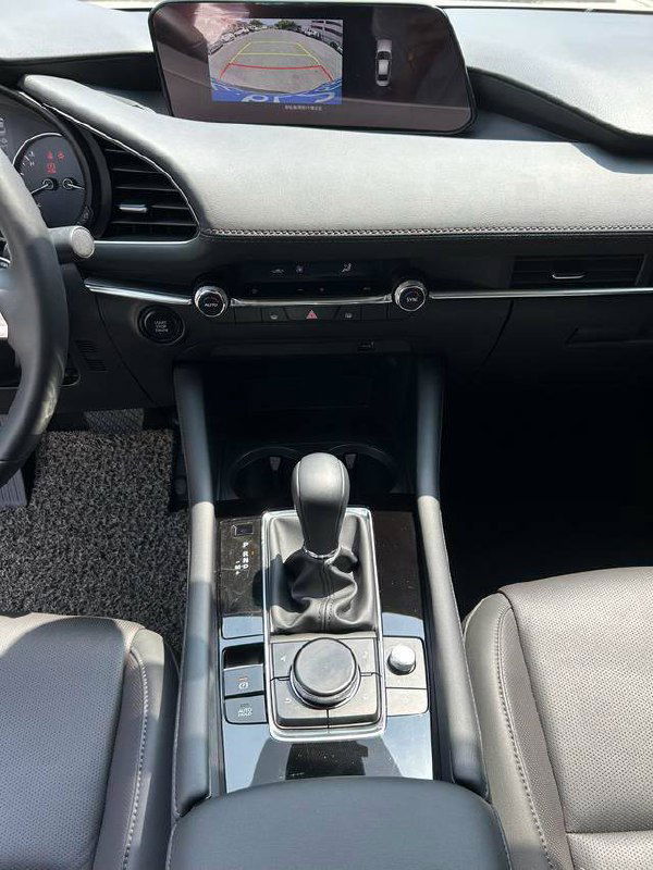 Крупный план центральной консоли и селектора АКПП в Mazda 3, видно органы управления мультимедиа и рычаг переключения передач.