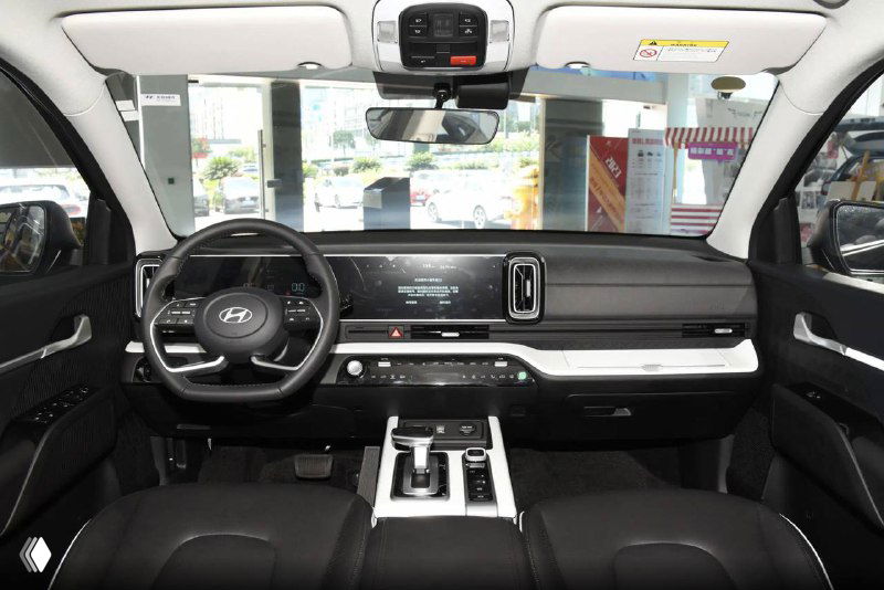 Панорамный вид салона Hyundai Mufasa: приборная панель и центральная консоль с большим экраном мультимедиа, строгий дизайн интерьера и чёрная обивка сидений.