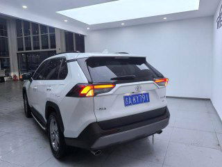 Фото белого Toyota RAV4 2020 года сзади в салоне дилера; задняя оптика, багажник и китайский регистрационный знак на фоне.