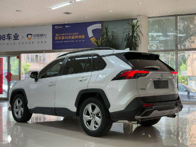 Фото Toyota RAV4 2021 сзади в выставочном зале; вид задней части, стоп-сигналы и общий фон шоурума на заднем плане.