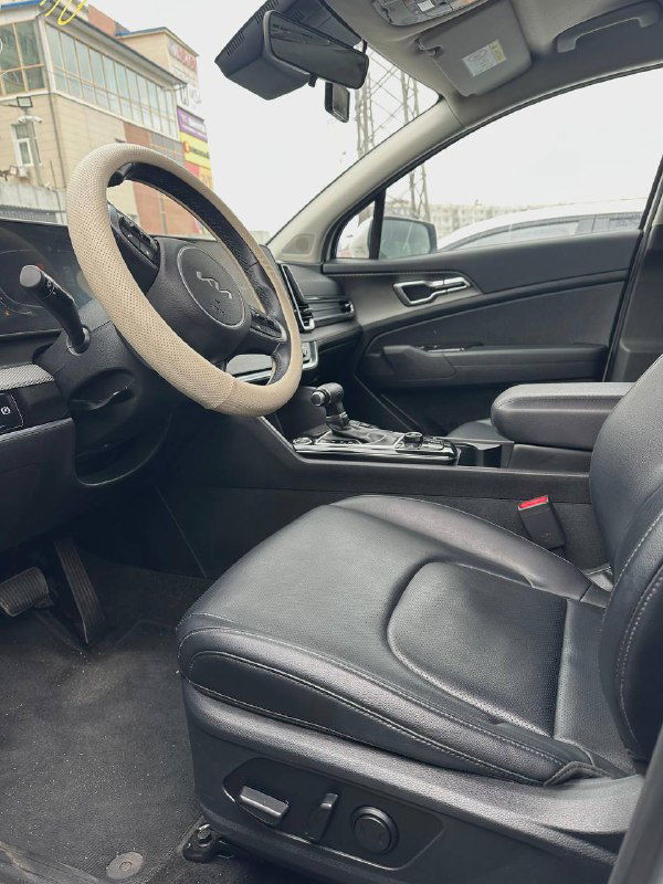 Вид на передние кресла KIA Sportage 2022: водительское сиденье с электроприводом и кожаная отделка, общий план салона с центральным тоннелем.