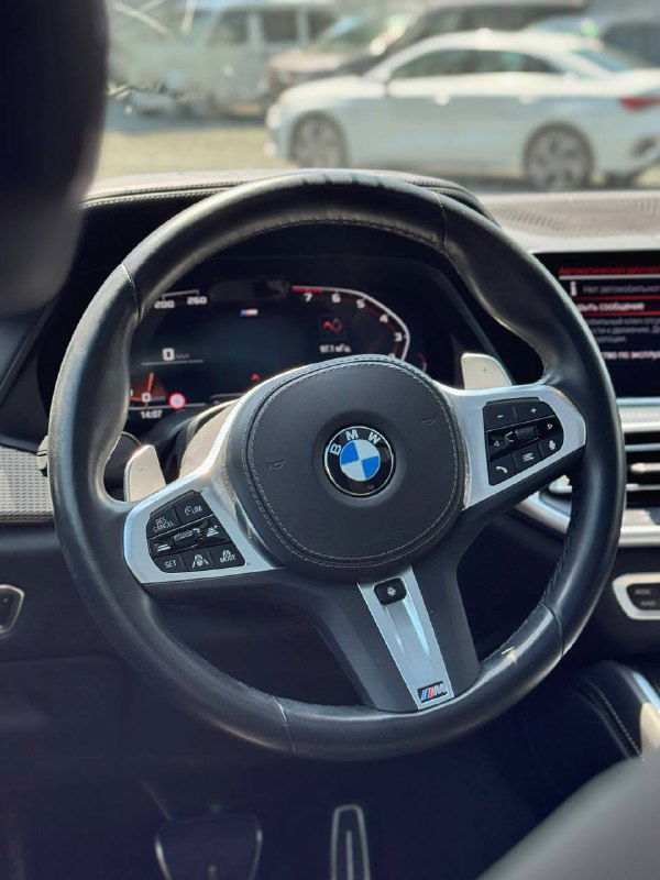 Рулевое колесо BMW с логотипом и аналоговой/цифровой комбинацией приборов — вид водителя на салон и переднее стекло.