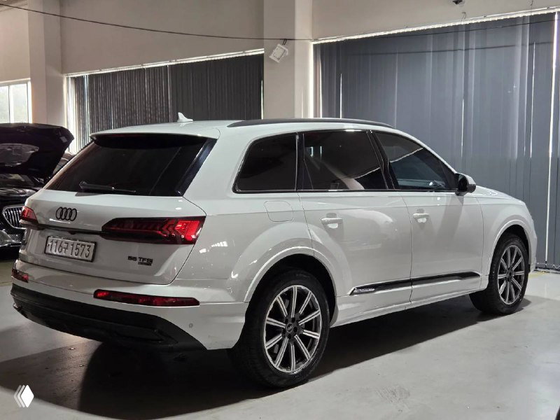 Задняя часть белого Audi Q7 45TFSI, вид со стороны кормы; видна задняя оптика, бампер и профиль автомобиля на площадке.
