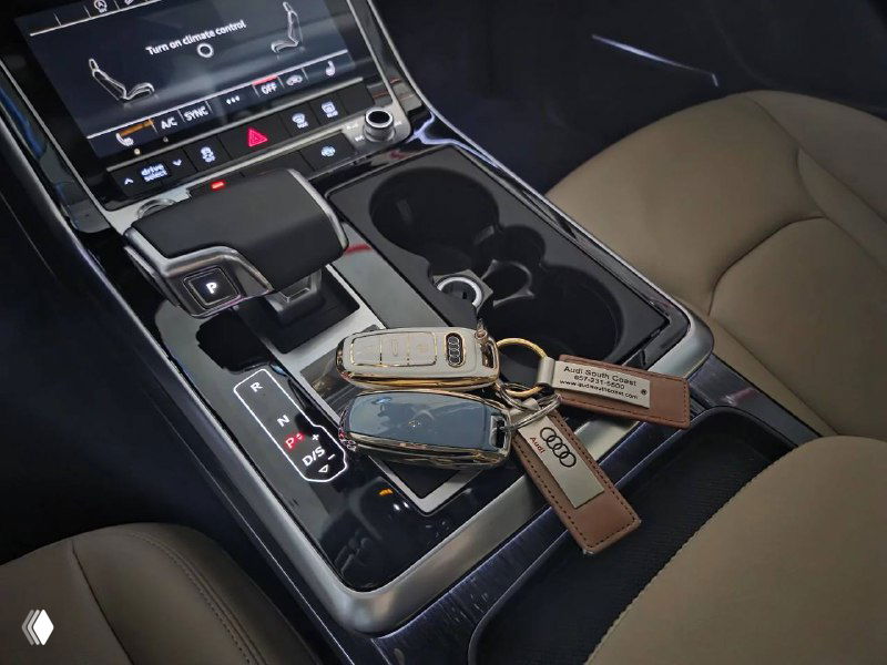 Крупный план центральной консоли Audi Q7 с подстаканниками и ключами автомобиля на переднем пассажирском месте.