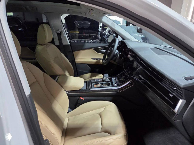 Передние сиденья Audi Q7 бежевого цвета, вид внутри салона со стороны дверного проёма; показана отделка и посадка водителя.