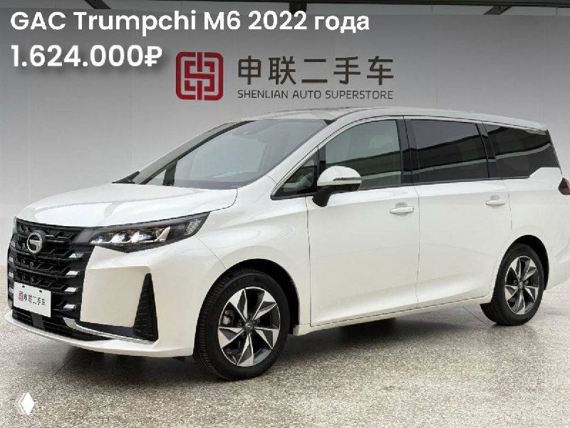 Белый GAC Trumpchi M6, фронтальный ракурс в салоне выставочного зала; подчёркнуты фары, форма капота и общий вид автомобиля в белом цвете.