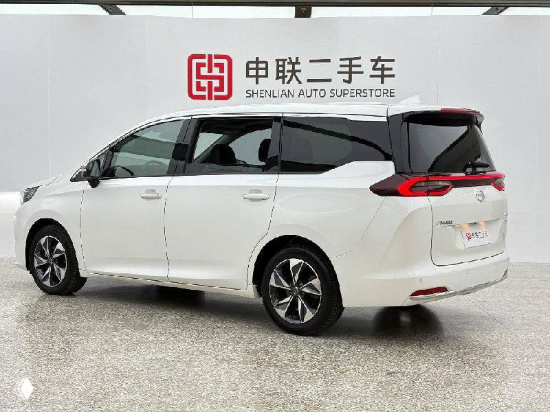 Белый GAC Trumpchi M6, боковой и задний вид на светлом фоне шоурума; видна линия кузова, стекла и колёсные диски на белом автомобиле.